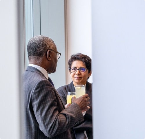At a Nedonboard networking event, two professionals in suits engage in a conversation over drinks, discussing business strategies and building connections.