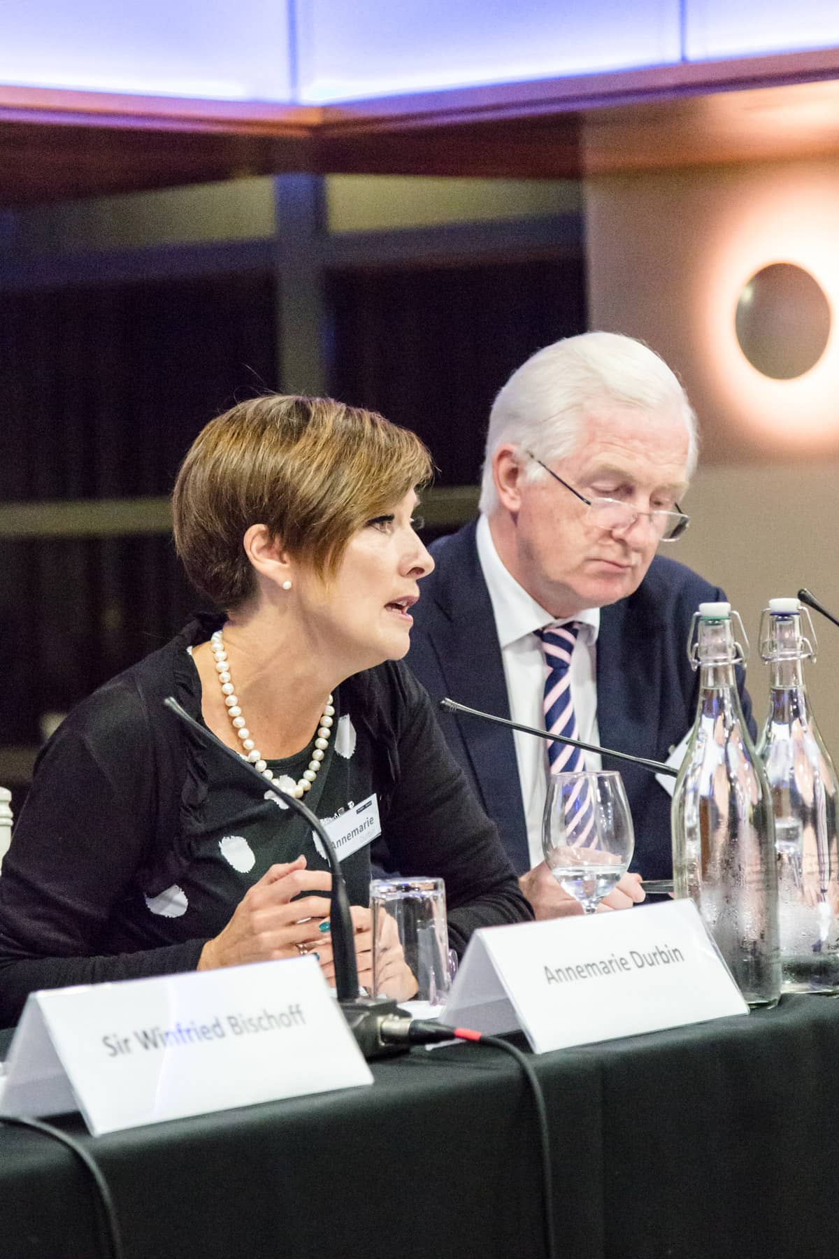 A man and woman from Nedonboard sitting at a table with microphones, engaged in a conversation or possibly conducting an interview.