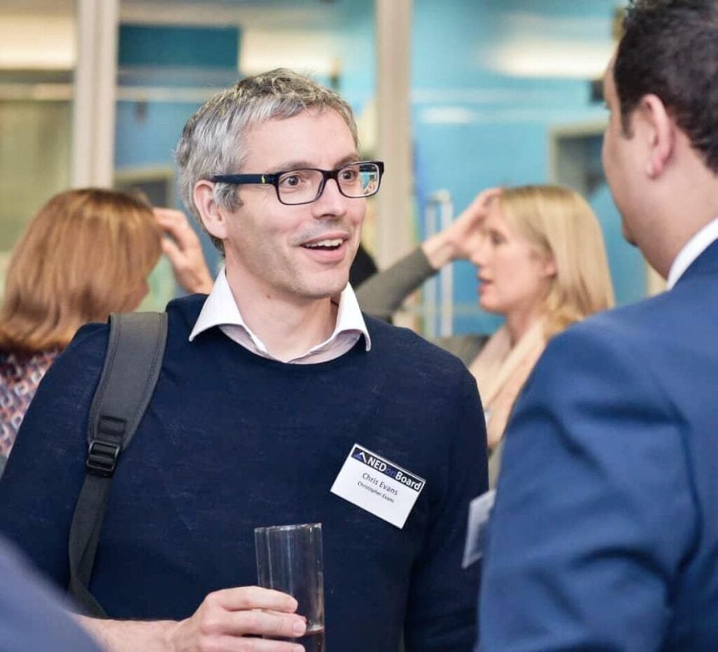 At a Nedonboard social gathering, a bespectacled man engages enthusiastically with a group of individuals, fostering discussions and connections.