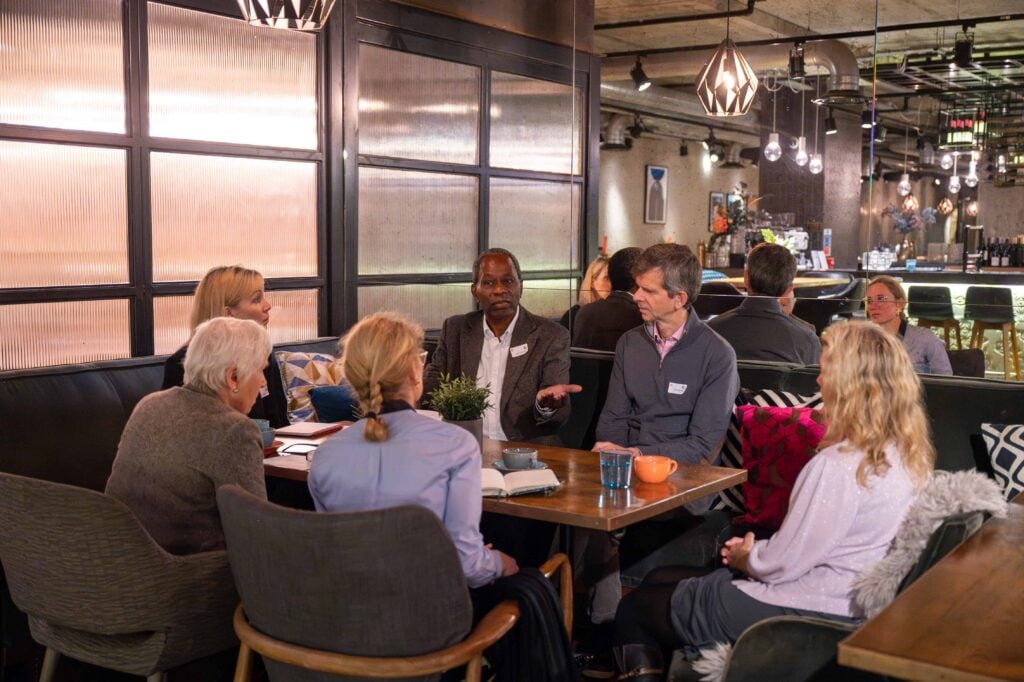 A group of people sit around a table in a dimly lit restaurant or cafe, engaged in conversation.
