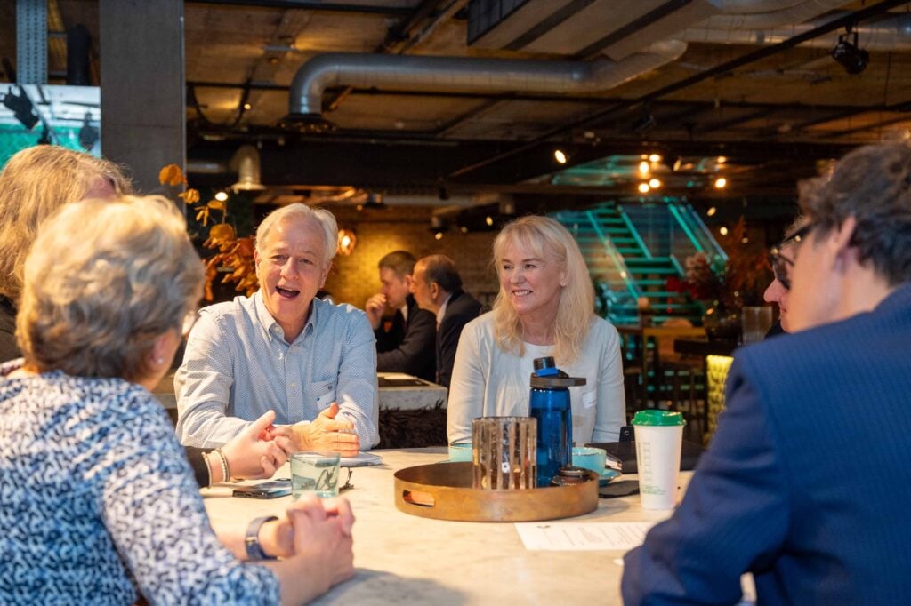 A group of people sit at a table having a discussion in a warmly lit, industrial-style setting